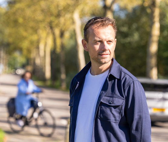 Foto van Jan-Cor, staande in een groene omgeving met een fietser op de achtergrond
